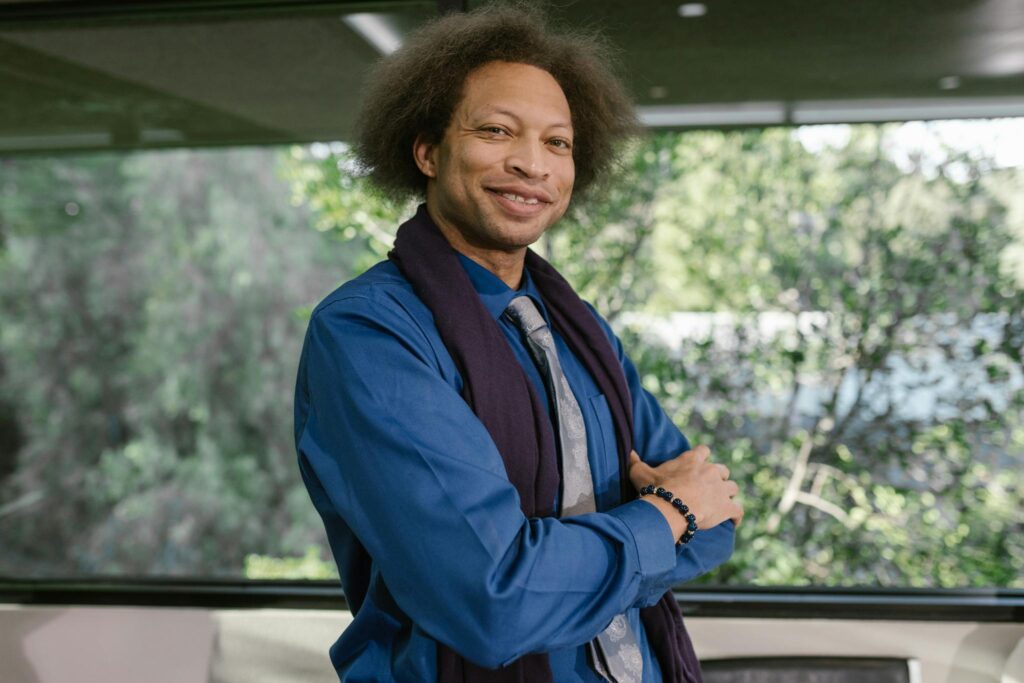 Smiling business professional posing confidently in a modern office with greenery outside.